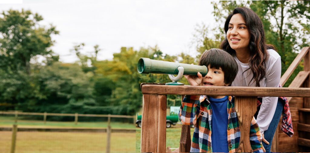 Photograph of a woman and her son looking through a playground spyglass.