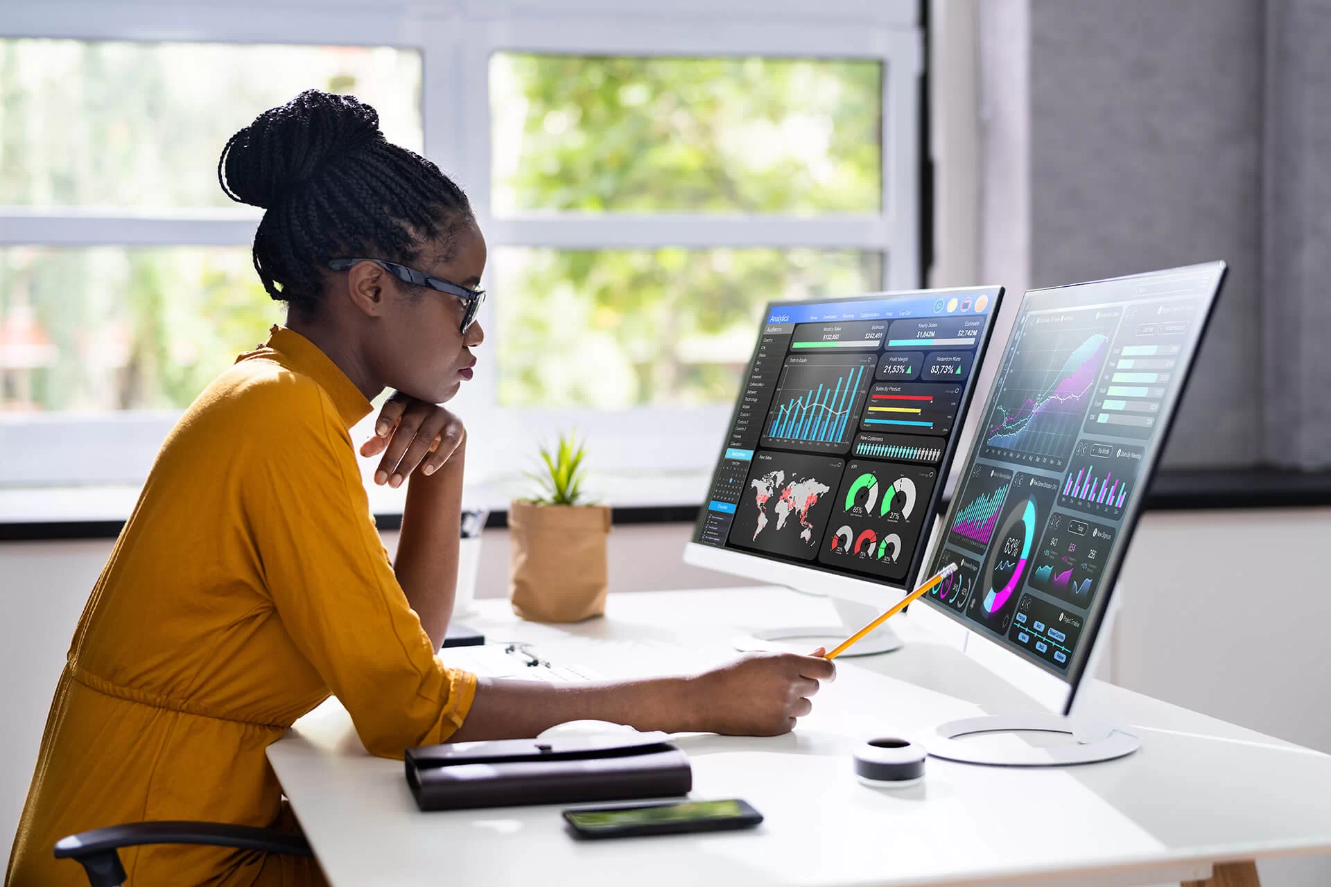 A woman looking at two computer monitors that have various data dashboards on them