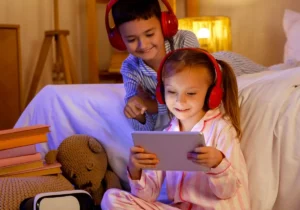 a young brother and sister watching a tablet with headphones on