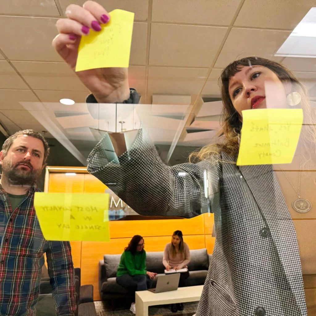 Photo of a man and a woman placing sticky notes on a glass wall.