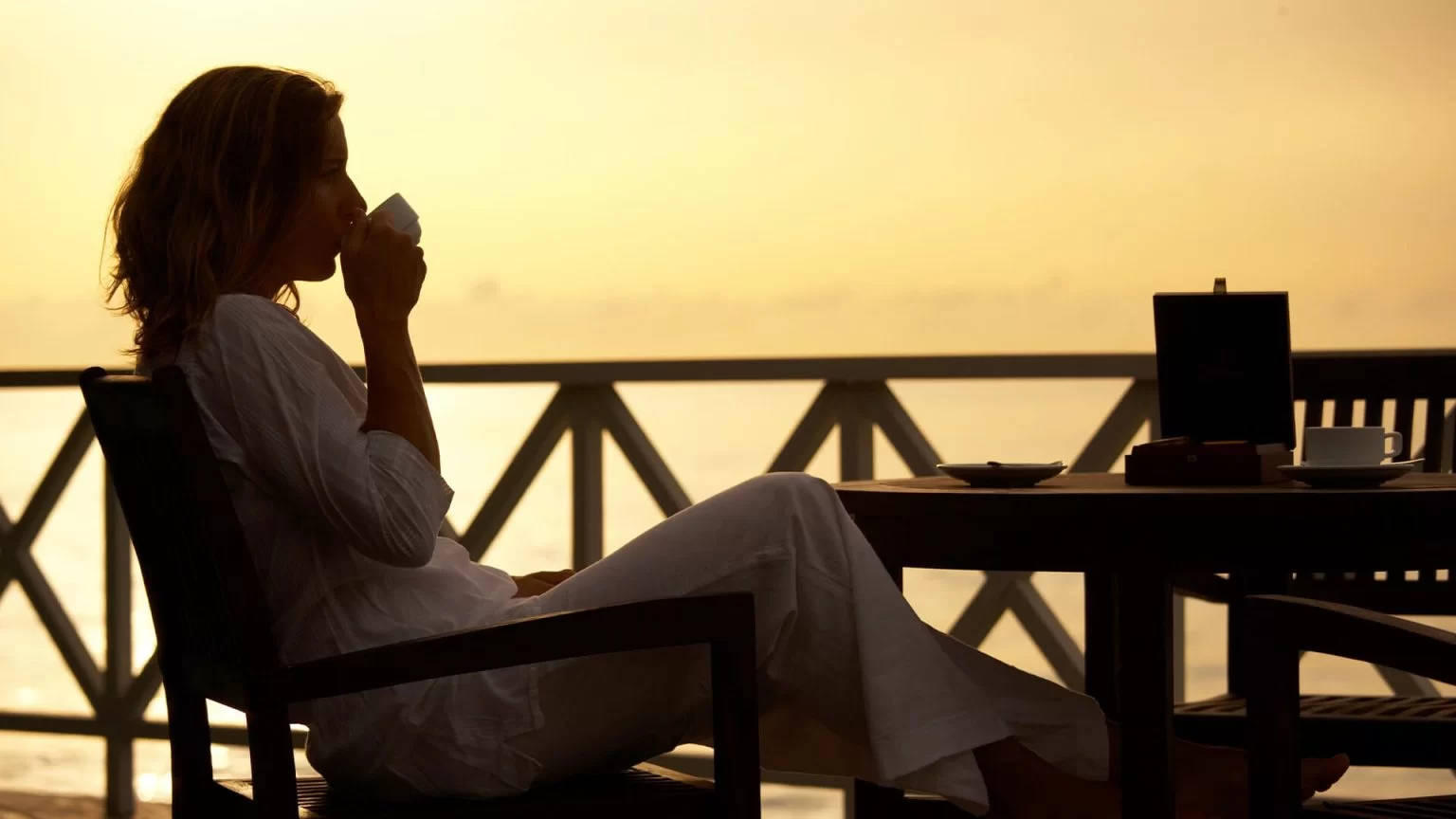 Women relaxing in a chair sipping coffee with a view of the water