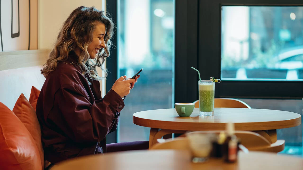 Woman smiling while looking at her phone in a cafe