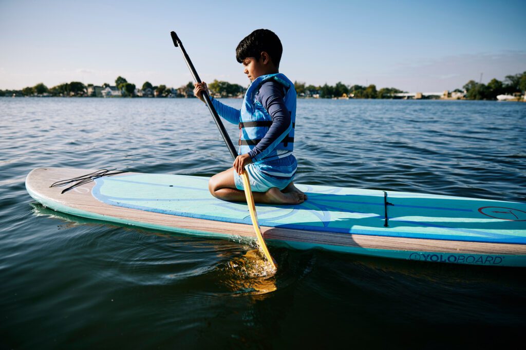 Photo of a young boy kneeling on a paddle board.