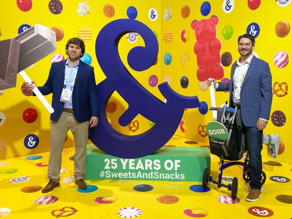 Ampersand selfie station with men posing with giant candy props