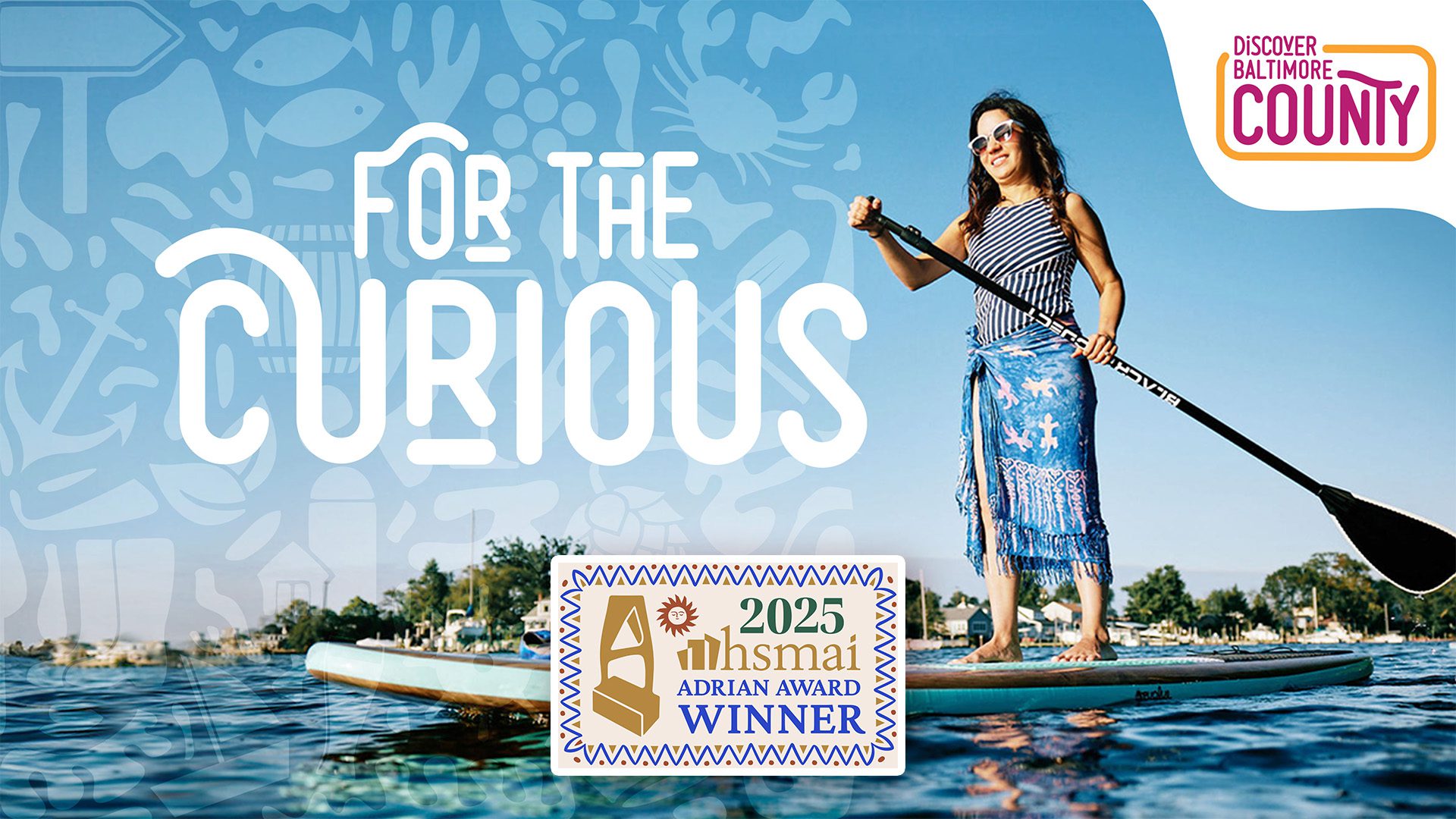 A paddleboarder on the water beside the “Discover Baltimore County” logo with large text reading “For the Curious” and a badge noting the 2025 HSMAI Adrian Award win for the Baltimore County Tourism rebrand.