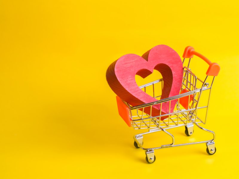 A supermarket trolley with a red heart inside. Love of shopping and shopping. Favorite store or supermarket. Buy love and happiness. Shopaholics, consumer society. Intimate services for money