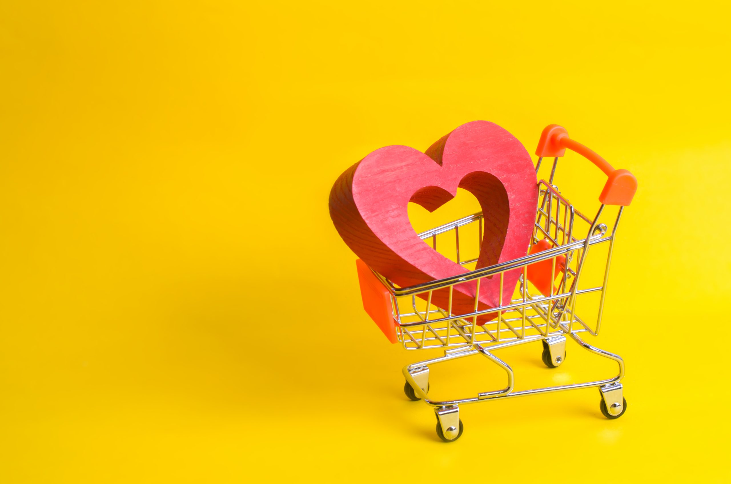 A supermarket trolley with a red heart inside. Love of shopping and shopping. Favorite store or supermarket. Buy love and happiness. Shopaholics, consumer society. Intimate services for money